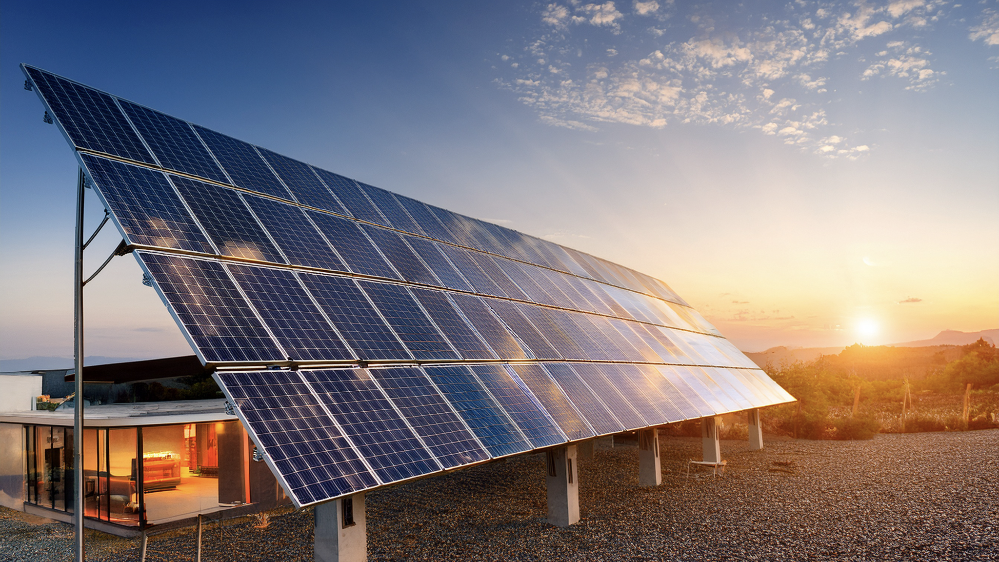Solar panels on a stand with a house in the background during sunset.