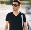 Man in black clothing with sunglasses and a backpack standing outdoors.